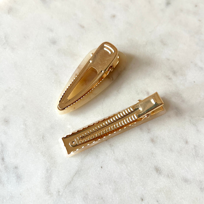 Two gold hair clips on a marble surface