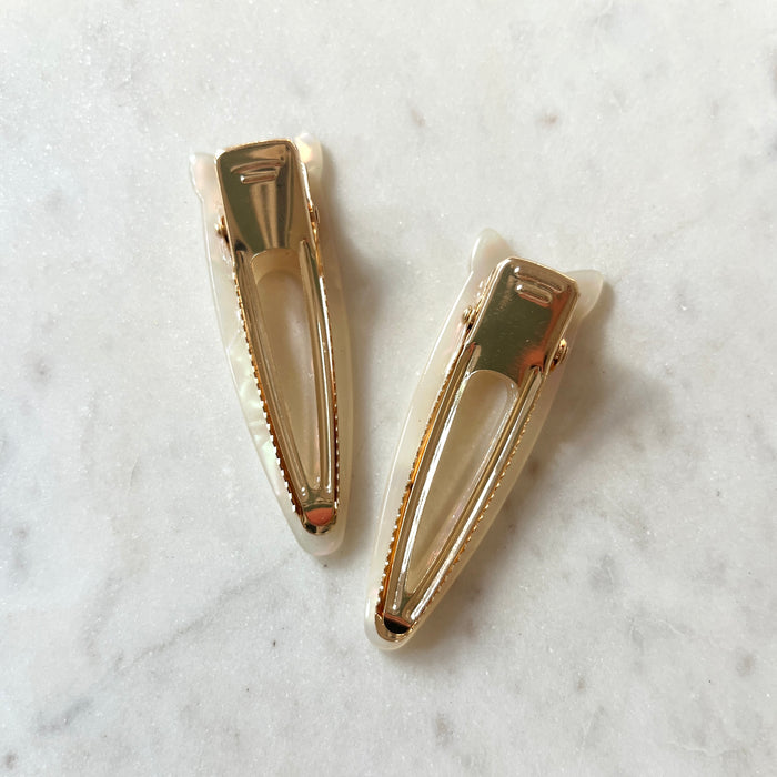 Two gold hair clips on a marble surface