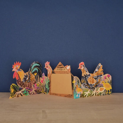 Three panels of a card with a rooster with a floral background shown unfolded on a wooden surface against a navy wall, shown from the back with middle panel displaying a 'message' text box