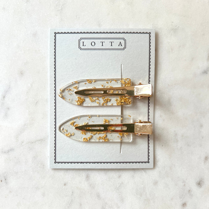 Two gold hair clips on a 'Lotta' branded card against a marble background