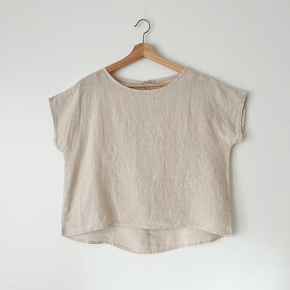A beige high-low hem linen tee hanging on a wooden hanger against a white wall.