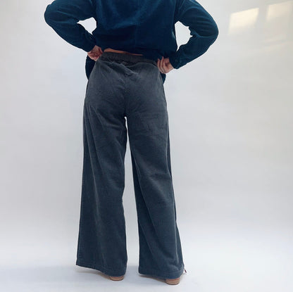 Model wearing Cut Loose Lux Corduroy Wide Leg Zip Pants in Gull, full back view against white studio backdrop showing deep slate blue-grey wide-wale corduroy, high-rise waistband, hands on hips, dramatically wide sweeping leg to ankle, styled with teal Cut Loose lux corduroy long shirt and tan leather cowboy boots