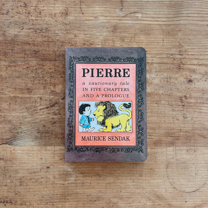 Front cover of Pierre: A Cautionary Tale in Five Chapters and a Prologue, a small board book by Maurice Sendak, displayed flat on a warm wood surface. The cover has a mottled dark gray background with an ornate black scrollwork border. A central salmon-pink panel bears the title "PIERRE" in large bold black lettering, with the subtitle "a cautionary tale / IN FIVE CHAPTERS / AND A PROLOGUE" in mixed italic and caps below. A rectangular illustration shows Pierre — a dark-haired boy in a blue jacket — facing