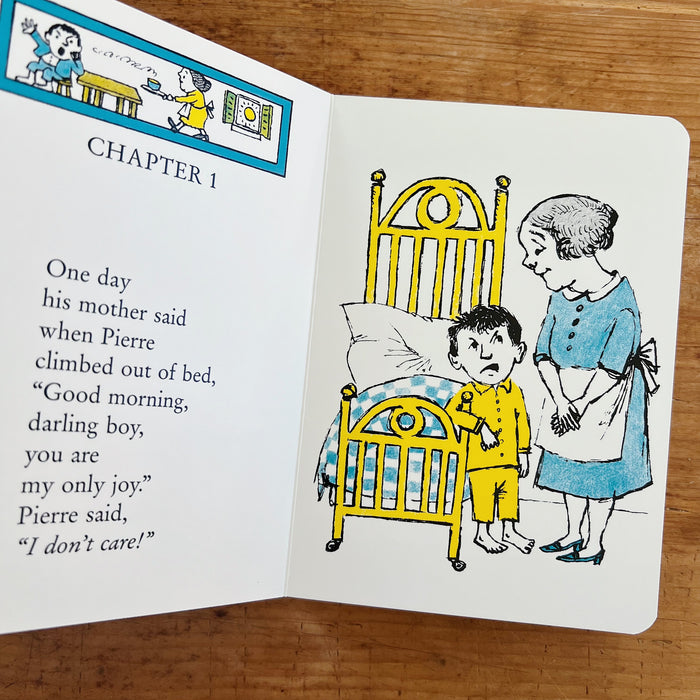 Open interior spread of Pierre board book displayed on a warm wood surface, showing Chapter 1. The left page has a small turquoise-bordered header illustration of a scene from the story, the chapter heading "CHAPTER 1" in bold black caps, and the verse text: "One day / his mother said / when Pierre / climbed out of bed, / 'Good morning, / darling boy, / you are / my only joy.' / Pierre said, / 'I don't care!'" The right page shows Maurice Sendak's full-color illustration of Pierre — a small boy in yellow pa