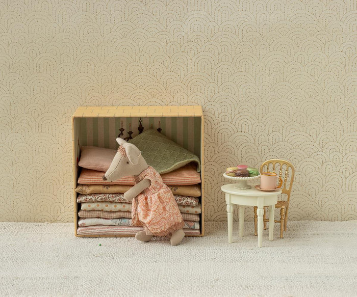 Maileg Princess and the Pea Big Sister Mouse — lifestyle scene of princess mouse doll in a pink lace dress resting on a stack of folded fabric mattresses inside the castle box, styled beside a miniature table with macarons and a gold chair