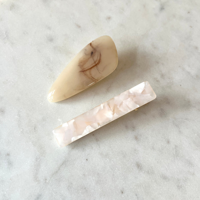 Two marbled beige and white hair clips on a marble surface