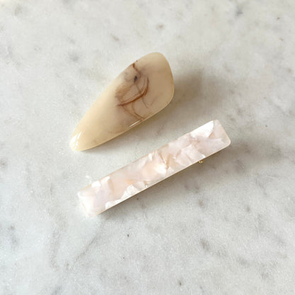 Two marbled beige and white hair clips on a marble surface