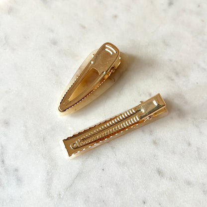 Two gold hair clips on a marble surface