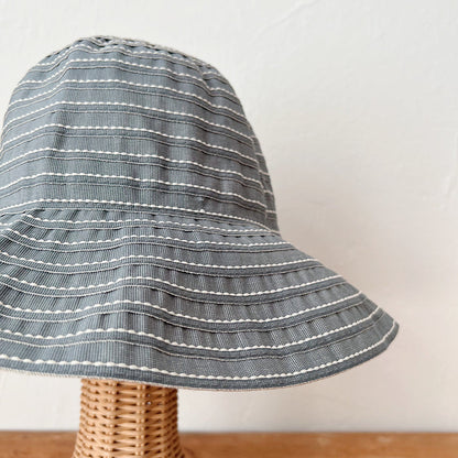 Close-up of sage ribbon hat fabric showing horizontal white running stitch detail across a wide floppy brim