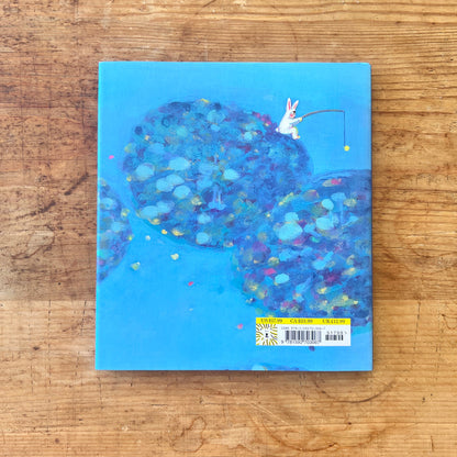 Back of the book cover with a colorful design and a rabbit on a blue background, placed on a wooden surface.