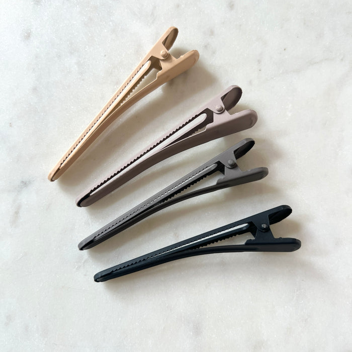 Set of four hair clips in beige, gray, and black on a marble surface
