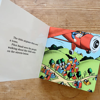 Interior spread of The Little Airplane showing Pilot Small leaning out of his red airplane as it flies over a colorful town below, beside text reading "The little airplane flies over a town. Pilot Small sees the people walking about like little ants on the streets below"