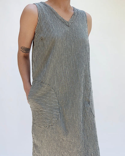 Person wearing a sleeveless, striped dress with a pocket on a plain background